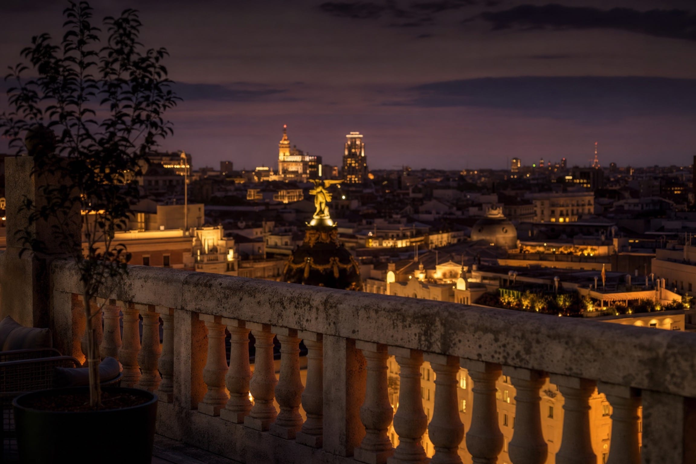 Madrid at blue hour seen from a private rooftop terrace, warm street lights below